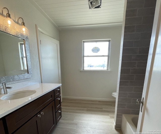 bathroom featuring toilet, a washtub, wood finished floors, baseboards, and vanity