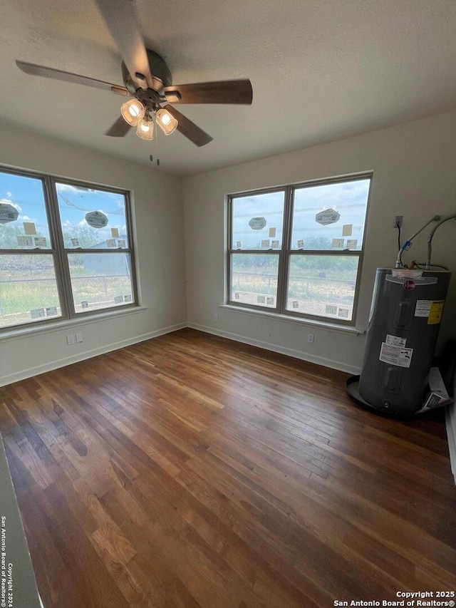 spare room featuring dark wood finished floors, baseboards, electric water heater, and a ceiling fan