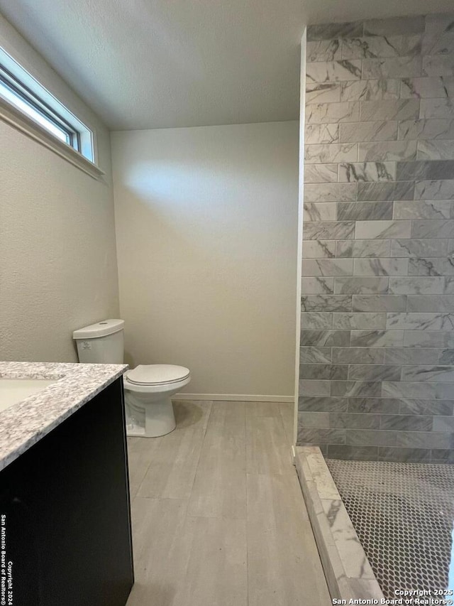 bathroom featuring baseboards, toilet, tiled shower, wood finished floors, and vanity