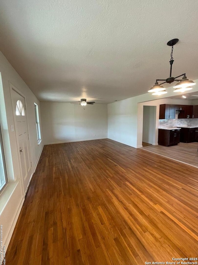 unfurnished living room featuring baseboards, a textured ceiling, wood finished floors, and a ceiling fan
