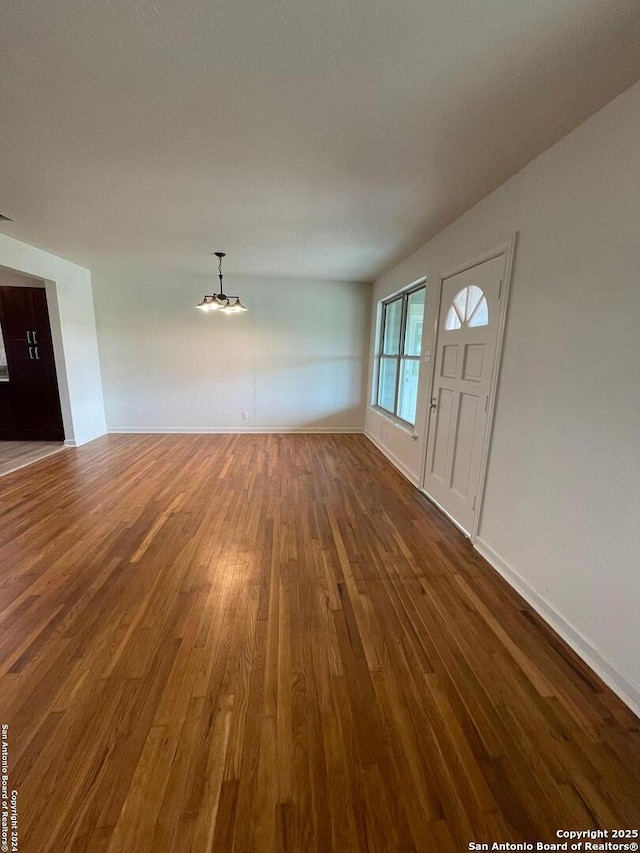 unfurnished living room featuring a notable chandelier, baseboards, and wood finished floors