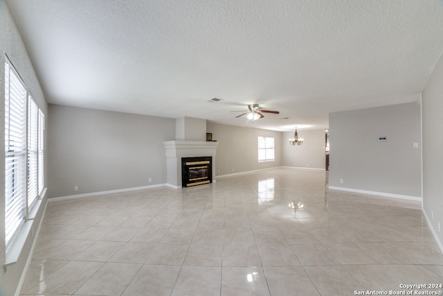 unfurnished living room featuring ceiling fan with notable chandelier, light tile patterned floors, and a textured ceiling