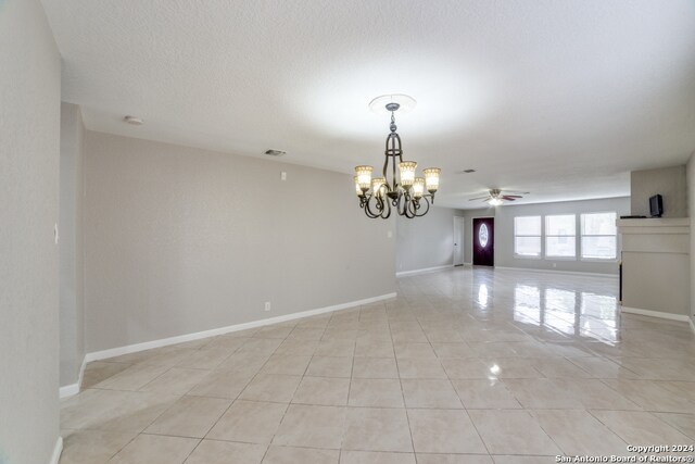 tiled empty room featuring ceiling fan with notable chandelier and a textured ceiling