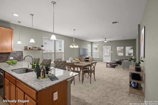 kitchen with decorative light fixtures, light stone countertops, sink, and light carpet