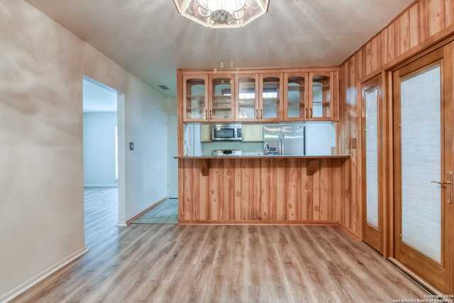 kitchen with light hardwood / wood-style flooring, a chandelier, kitchen peninsula, wood walls, and appliances with stainless steel finishes