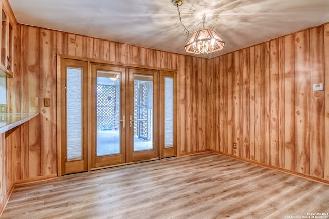 empty room with light hardwood / wood-style floors, an inviting chandelier, french doors, and wooden walls