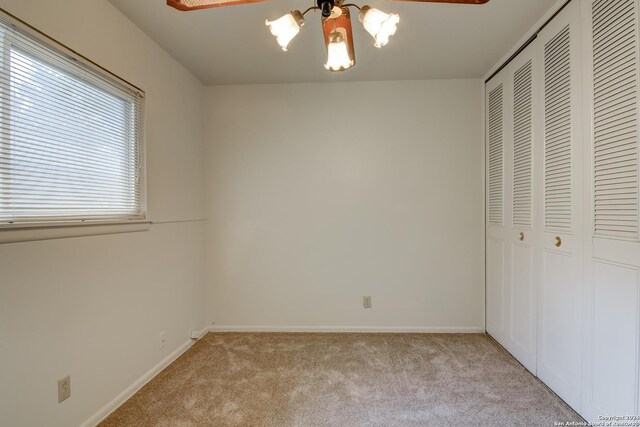 unfurnished bedroom with ceiling fan with notable chandelier, light carpet, and a closet