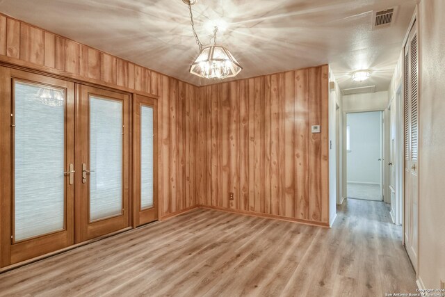 unfurnished room featuring wood walls, french doors, hardwood / wood-style flooring, and a notable chandelier