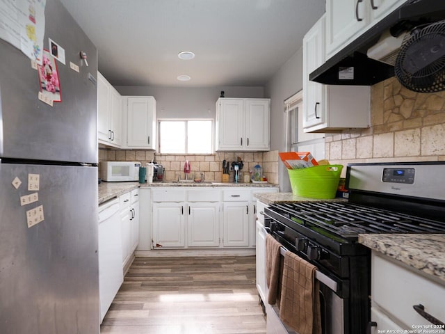 kitchen with appliances with stainless steel finishes, white cabinetry, light stone countertops, and extractor fan