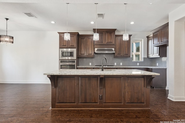 kitchen featuring range hood, decorative light fixtures, appliances with stainless steel finishes, and a kitchen island with sink