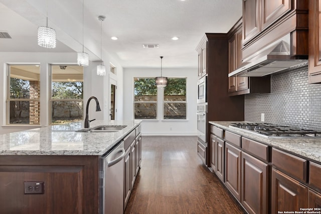 kitchen featuring dark wood-type flooring, a kitchen island with sink, decorative light fixtures, and stainless steel appliances