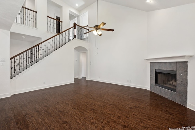 unfurnished living room featuring ceiling fan, a high ceiling, dark hardwood / wood-style flooring, and a tiled fireplace