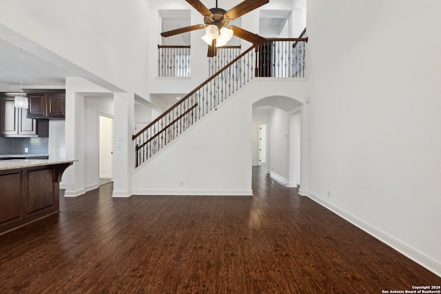 unfurnished living room with a high ceiling, ceiling fan, and dark hardwood / wood-style flooring