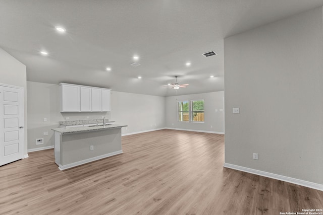 kitchen featuring ceiling fan, light stone counters, white cabinets, a center island with sink, and light wood-type flooring