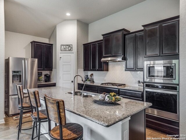 kitchen with sink, light wood-type flooring, decorative backsplash, a center island with sink, and appliances with stainless steel finishes