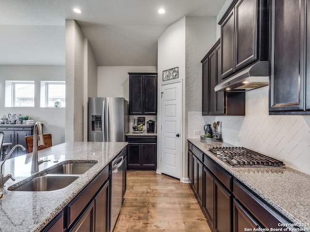 kitchen featuring appliances with stainless steel finishes, light stone counters, dark brown cabinets, sink, and light hardwood / wood-style flooring