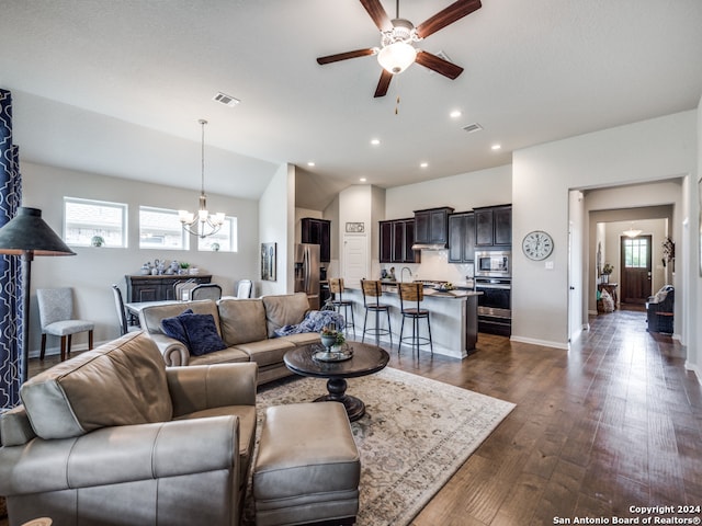 living room featuring ceiling fan with notable chandelier, dark hardwood / wood-style flooring, and vaulted ceiling