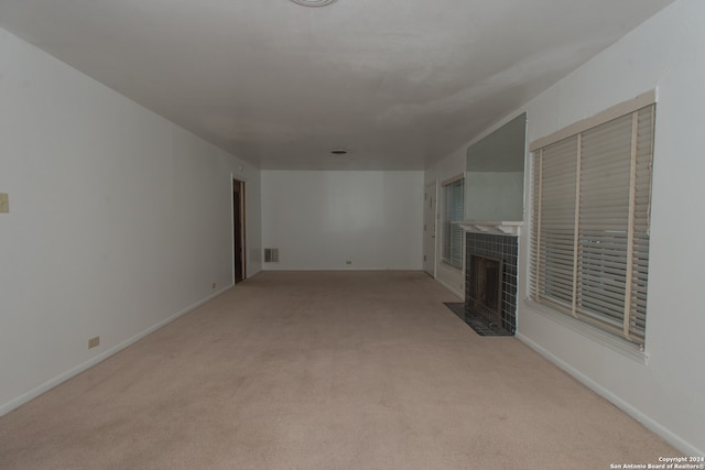 unfurnished living room featuring a tile fireplace and light colored carpet