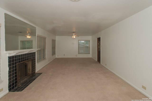 unfurnished living room with a tile fireplace, ceiling fan, and carpet flooring