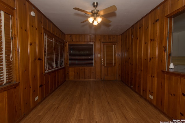 empty room featuring wooden walls, light wood-type flooring, and ceiling fan