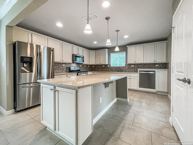 kitchen with stainless steel appliances, light stone countertops, a kitchen island, and white cabinets