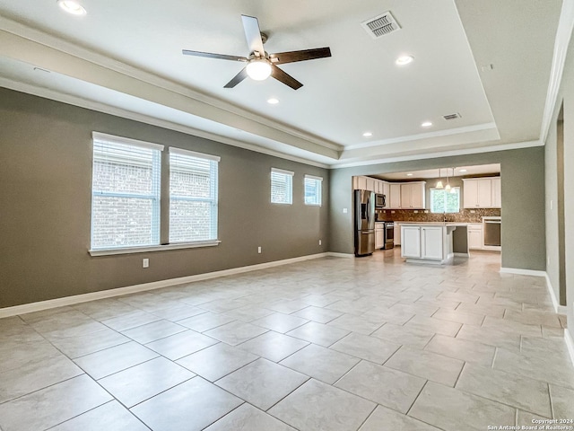 unfurnished living room featuring ceiling fan, a tray ceiling, ornamental molding, and a healthy amount of sunlight