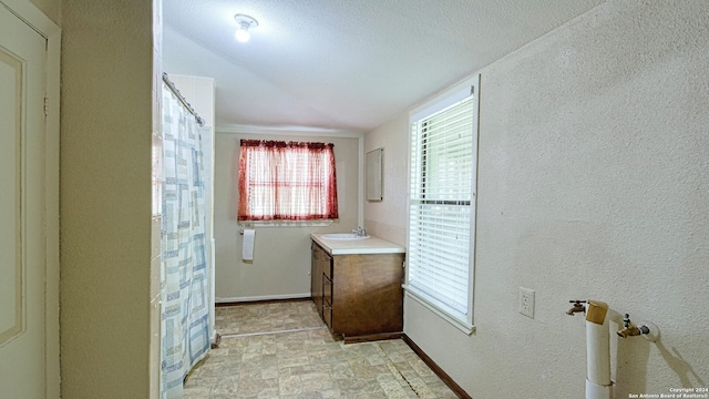 bathroom with vaulted ceiling, vanity, a textured ceiling, and tile patterned floors