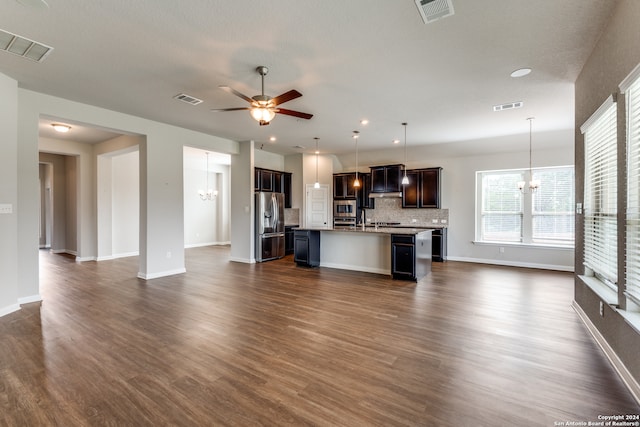 kitchen with decorative light fixtures, ceiling fan with notable chandelier, a kitchen breakfast bar, an island with sink, and dark wood-type flooring