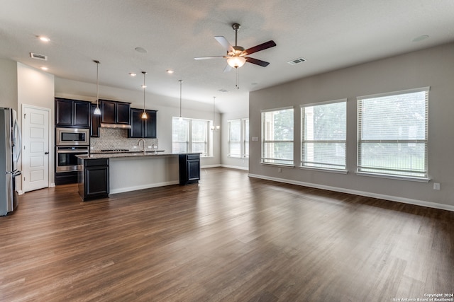 kitchen with stainless steel appliances, a center island with sink, decorative backsplash, dark hardwood / wood-style floors, and ceiling fan