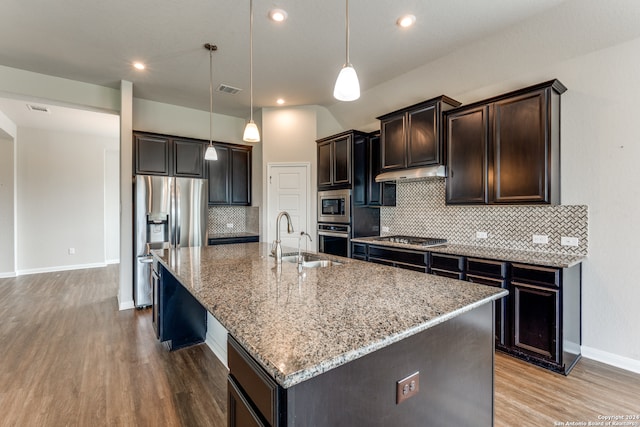 kitchen featuring light hardwood / wood-style flooring, stainless steel appliances, backsplash, dark brown cabinetry, and an island with sink