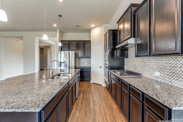 kitchen featuring appliances with stainless steel finishes, light wood-type flooring, tasteful backsplash, and decorative light fixtures