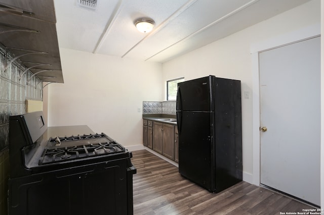 kitchen with range with gas cooktop, dark brown cabinets, wood-type flooring, and black fridge