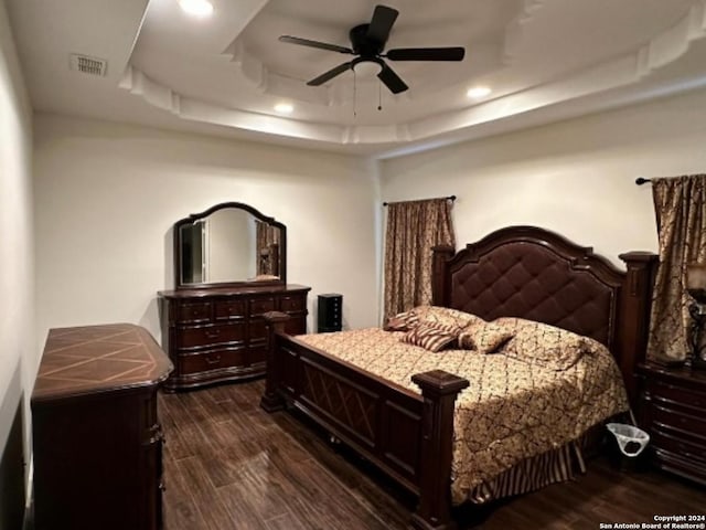 bedroom featuring dark hardwood / wood-style flooring, ceiling fan, and a raised ceiling