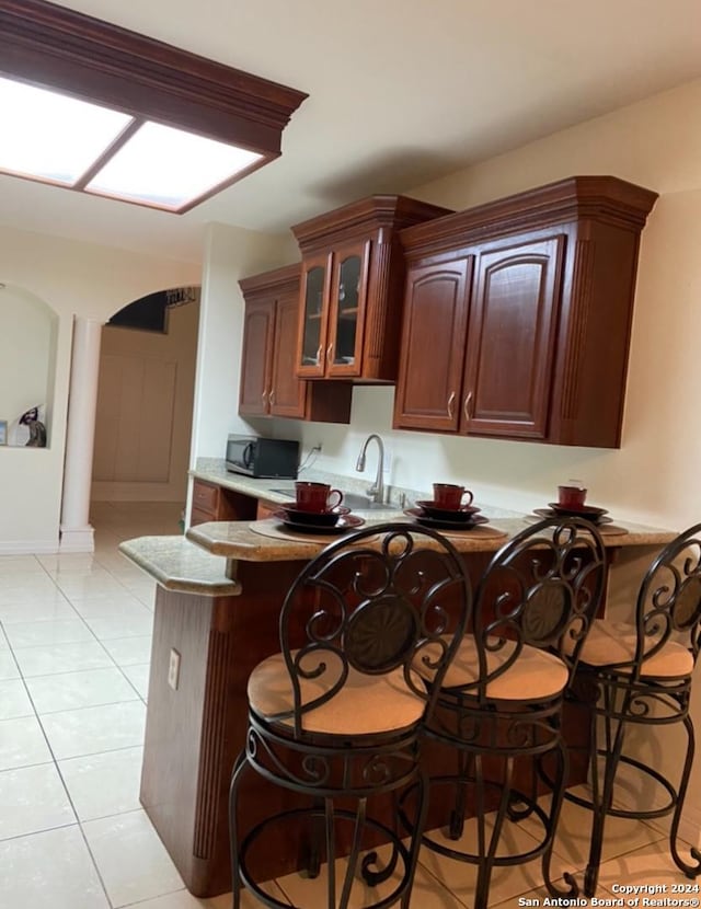 kitchen with kitchen peninsula, sink, a breakfast bar area, and light tile patterned floors