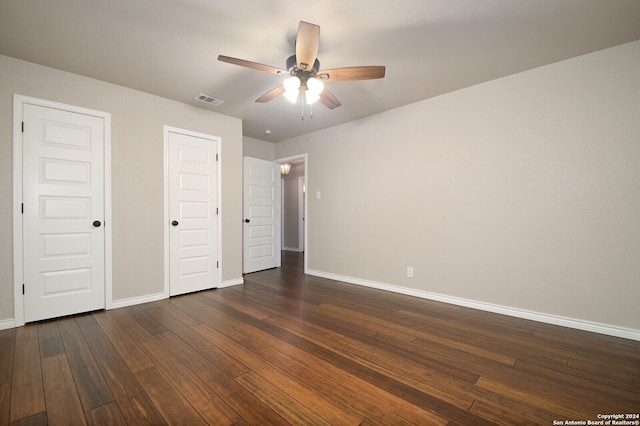 unfurnished bedroom with dark wood-type flooring, ceiling fan, and multiple closets