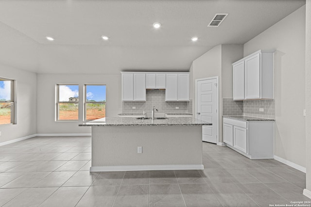 kitchen with light tile patterned flooring, a kitchen island with sink, and light stone counters