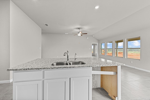 kitchen featuring vaulted ceiling, white cabinetry, sink, an island with sink, and light stone counters