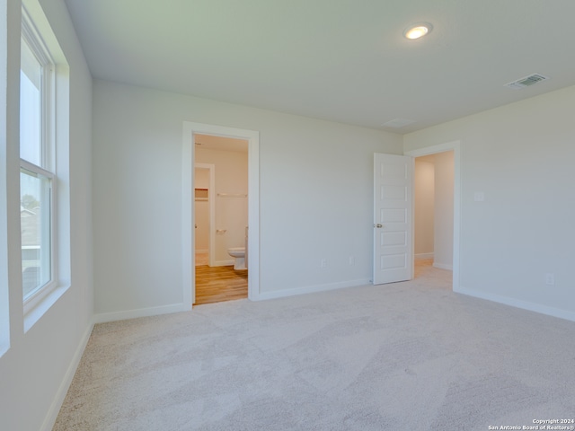 unfurnished bedroom featuring a closet, light colored carpet, a spacious closet, and ensuite bath