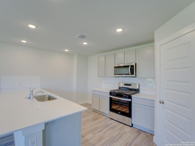 kitchen featuring kitchen peninsula, light hardwood / wood-style flooring, sink, backsplash, and stainless steel appliances