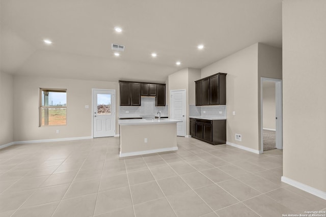 kitchen with a kitchen island with sink, light tile patterned floors, decorative backsplash, sink, and lofted ceiling