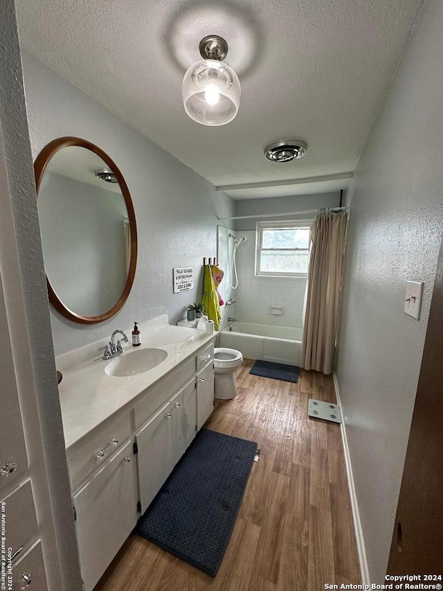 full bathroom with hardwood / wood-style floors, shower / bath combo with shower curtain, a textured ceiling, toilet, and vanity