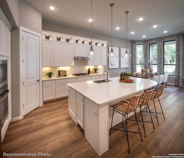 kitchen with sink, white cabinets, dark wood-type flooring, and an island with sink