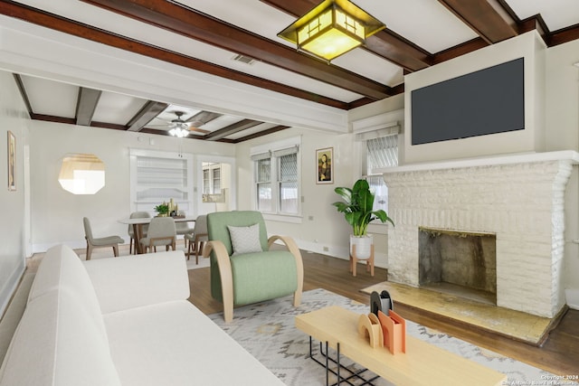 living room with beamed ceiling, a brick fireplace, a healthy amount of sunlight, and hardwood / wood-style floors