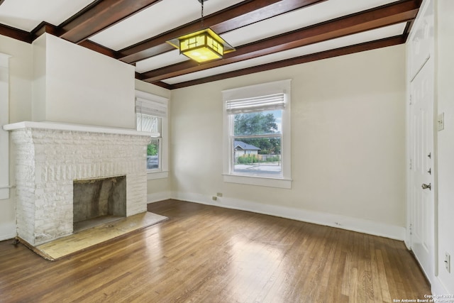 unfurnished living room featuring hardwood / wood-style floors, beamed ceiling, and a brick fireplace