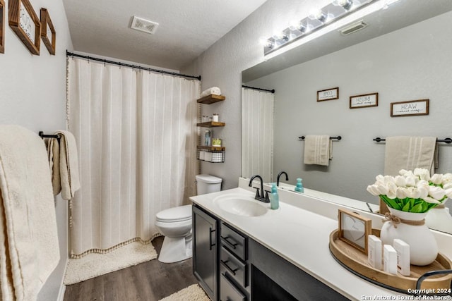 bathroom featuring toilet, a textured ceiling, wood-type flooring, walk in shower, and vanity