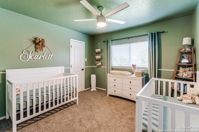 bedroom featuring ceiling fan, light colored carpet, a textured ceiling, and a nursery area