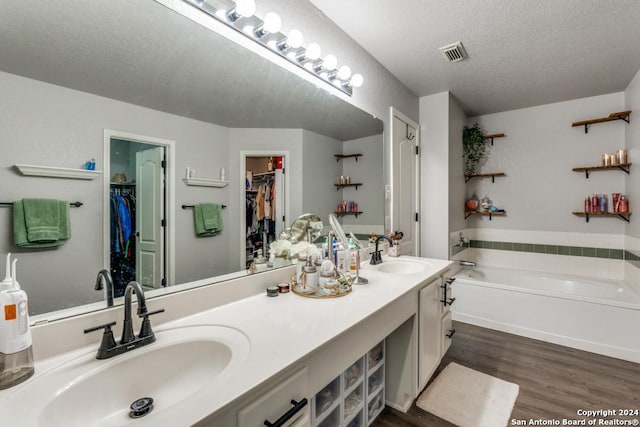 bathroom with hardwood / wood-style floors, a textured ceiling, a bath, and vanity