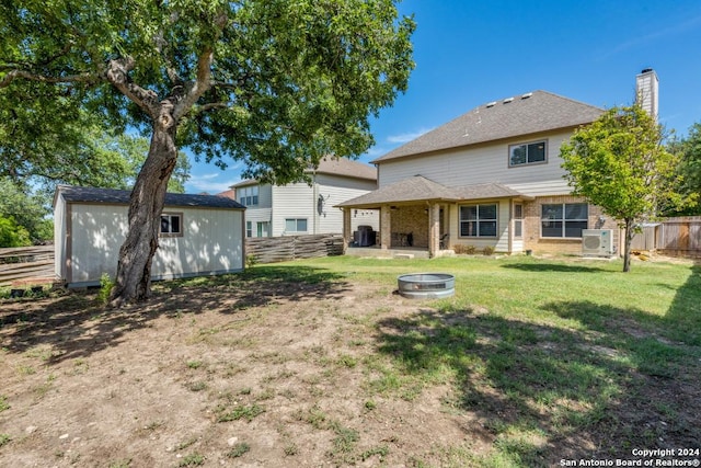 rear view of property with a shed, ac unit, a yard, and a fire pit