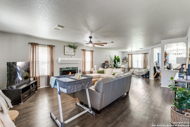 living room with ceiling fan with notable chandelier, a healthy amount of sunlight, dark hardwood / wood-style floors, and a textured ceiling