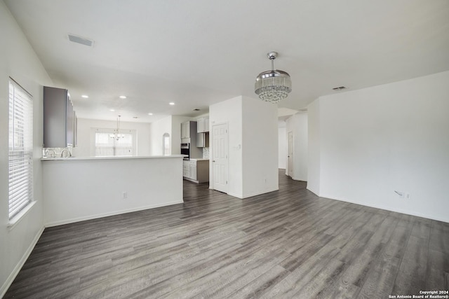 unfurnished living room featuring dark hardwood / wood-style flooring, a healthy amount of sunlight, and a chandelier